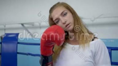 拳击场上的运动女孩在拳击手套上准确地打拳，在锻炼时看着摄像机